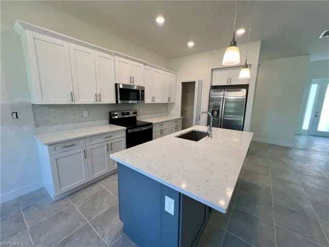 Kitchen with white cabinetry, sink, hanging light fixtures, stainless steel appliances, and an island with sink and QUARTZ TOPS.