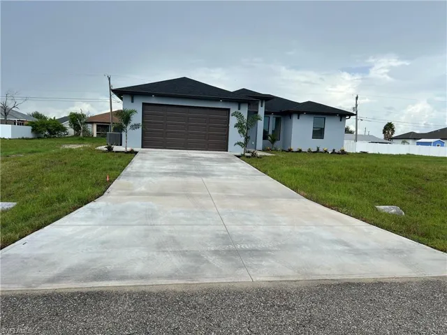 View of front of property featuring a garage, driveway, a front lawn, and stucco siding