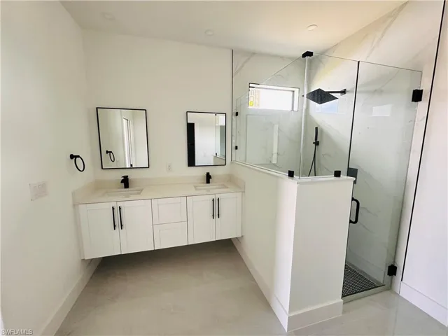 Bathroom featuring double vanity, marble finish floor, a marble finish shower, and a sink