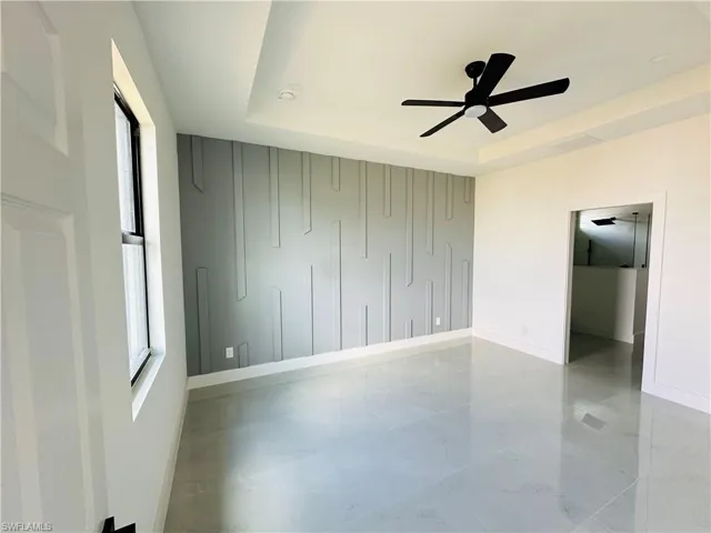Spare room featuring a raised ceiling, ceiling fan, marble finish floor, and baseboards