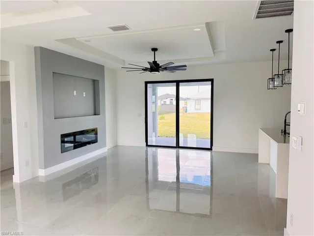 Unfurnished living room with a tray ceiling, a glass covered fireplace, visible vents, and baseboards