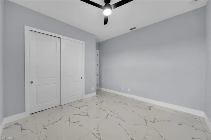 Unfurnished bedroom featuring light marble finish floors, a closet, and a ceiling fan