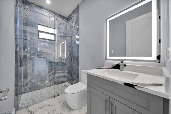 Bathroom with marble tiled floors, vanity, a marble finish shower, and recessed lighting