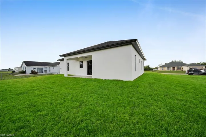 Rear view of house with stucco siding, a lawn, a ceiling fan, and a patio area