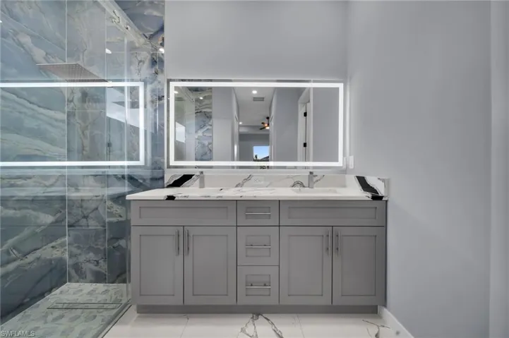 Full bath with a marble finish shower, double vanity, and marble look tiles