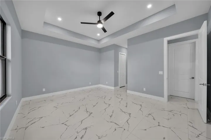 Unfurnished bedroom with a raised ceiling, recessed lighting, a ceiling fan, light marble finish flooring, and a closet