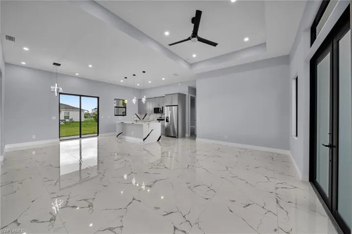 Unfurnished living room with a ceiling fan, a raised ceiling, recessed lighting, and light marble finish floors