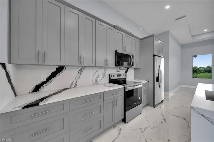 Kitchen featuring appliances with stainless steel finishes, gray cabinetry, light marble finish floors, recessed lighting, and light stone counters