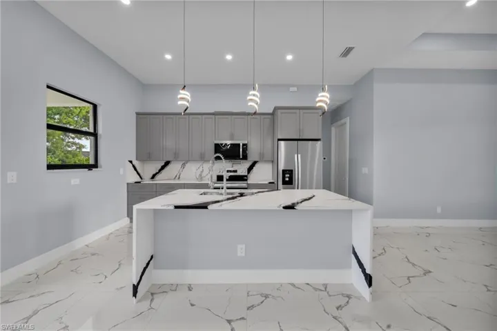 Kitchen featuring stainless steel appliances, gray cabinets, light marble finish floors, a center island with sink, and recessed lighting