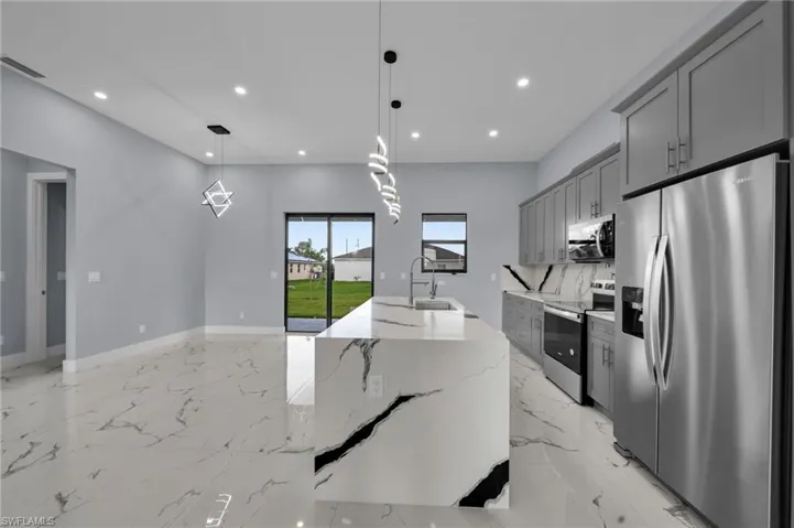 Kitchen with stainless steel appliances, gray cabinets, recessed lighting, light marble finish floors, and a center island with sink