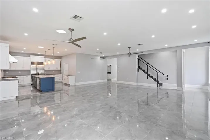 Spacious interior featuring a contemporary kitchen with a blue island, stainless steel appliances, white cabinetry, and pendant lighting