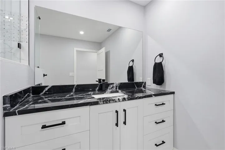 Contemporary bathroom vanity featuring a black patterned countertop, white cabinetry with black hardware, and a large wall-mounted mirror