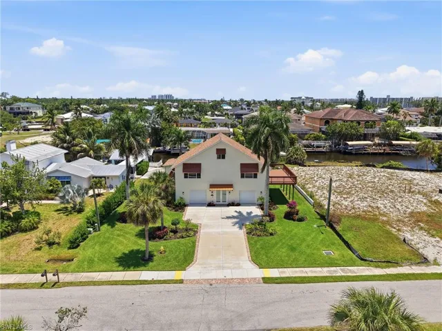 Two-story residence featuring a paved driveway, attached two-car garage, and a waterfront location with an expansive open deck