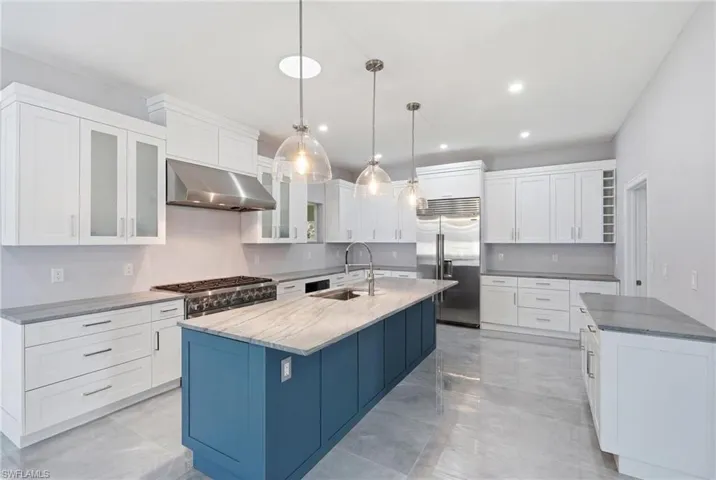 Spacious kitchen featuring an expansive central island with a contrasting blue finish, stone countertop, and integrated sink