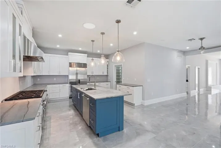 Modern kitchen featuring a blue island with sink, white perimeter cabinetry, stainless steel appliances, and light-toned countertops