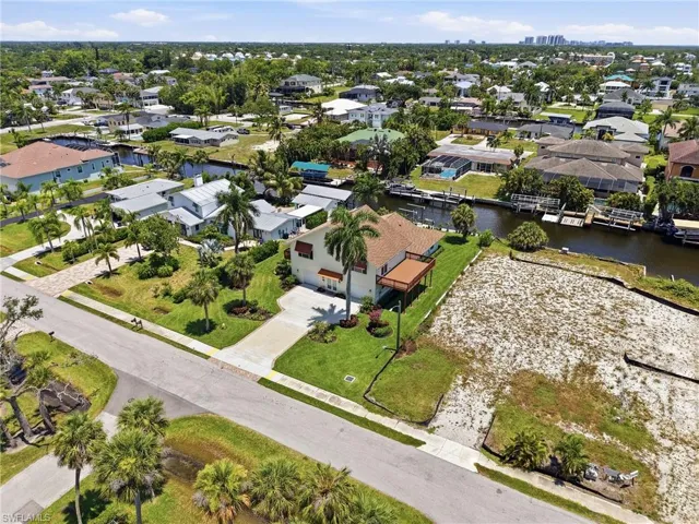 Waterfront property featuring a two-story residence with a balcony, manicured lawn, and mature palm trees
