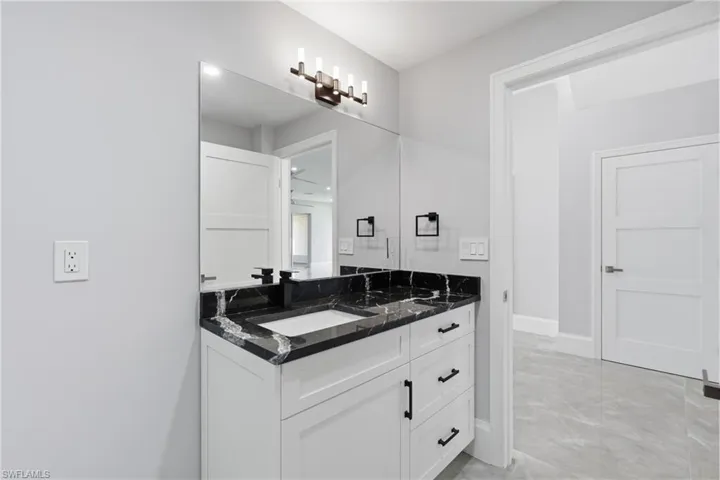 Contemporary bathroom vanity featuring a white shaker-style cabinet, black veined countertop, integrated rectangular sink, and matte black hardware