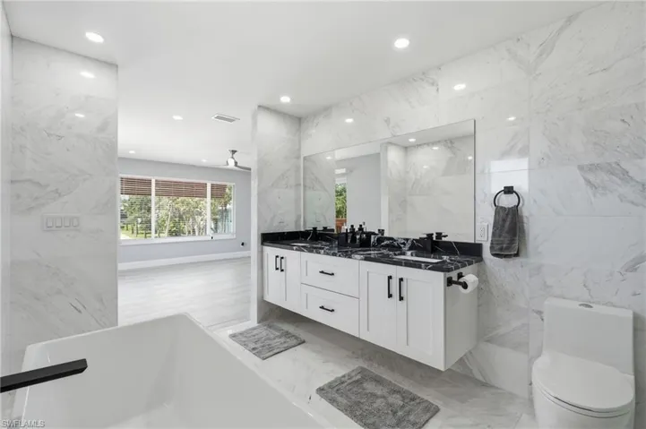 Contemporary bathroom featuring a floating dual vanity with black countertops, a deep soaking tub with a matte black faucet, and a wall-mounted toilet