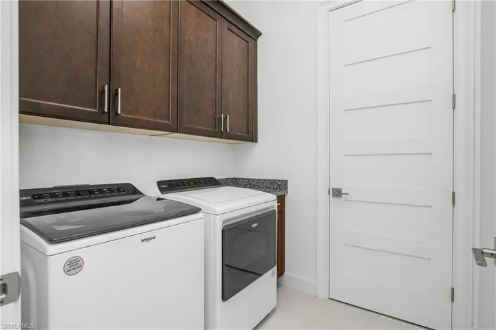 Laundry area with cabinets, light tile patterned floors, and washer and clothes dryer.