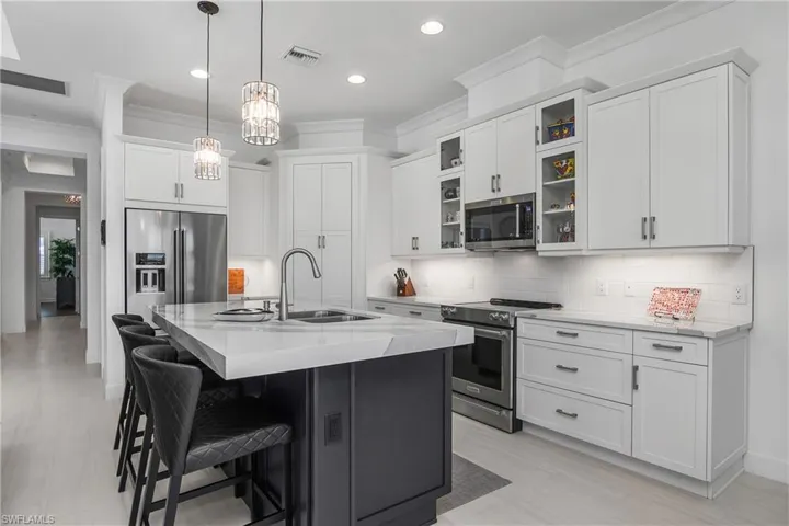 Kitchen with high end appliances, a kitchen island with sink, white cabinets, sink, and light quartz counters, accented with a 3" Edge.