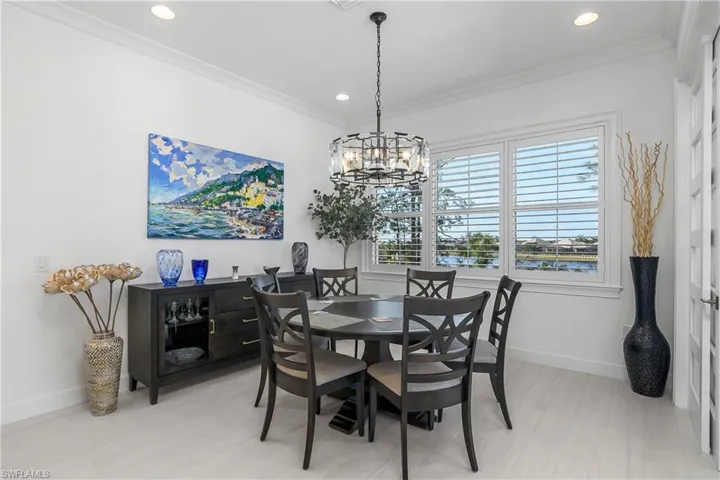 Dining space with ornamental molding and a notable chandelier. Plantation shutters. 7 x 48 porcelain tile Plank Style flooring. Crown molding.