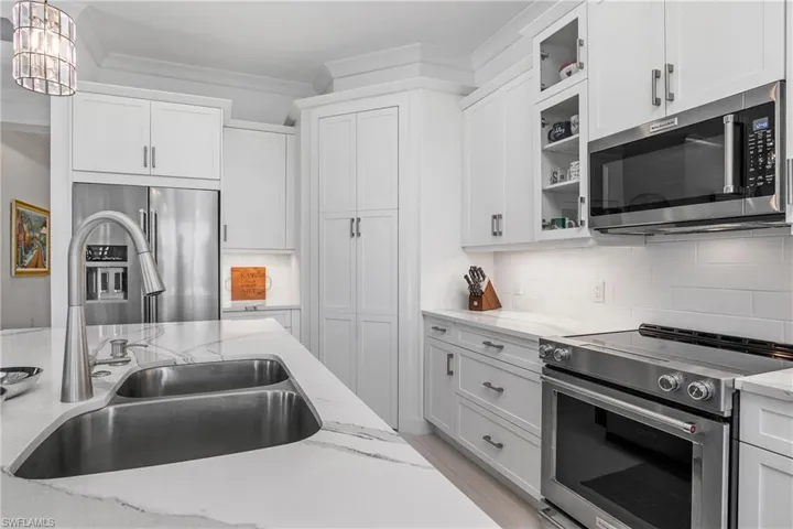 Kitchen with white cabinetry, sink, hanging light fixtures, decorative backsplash, and appliances with stainless steel finishes. White tile backsplash.