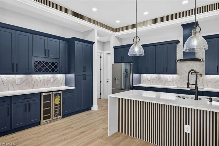 Kitchen with decorative backsplash, blue cabinetry, light stone counters, wine cooler, and recessed lighting
