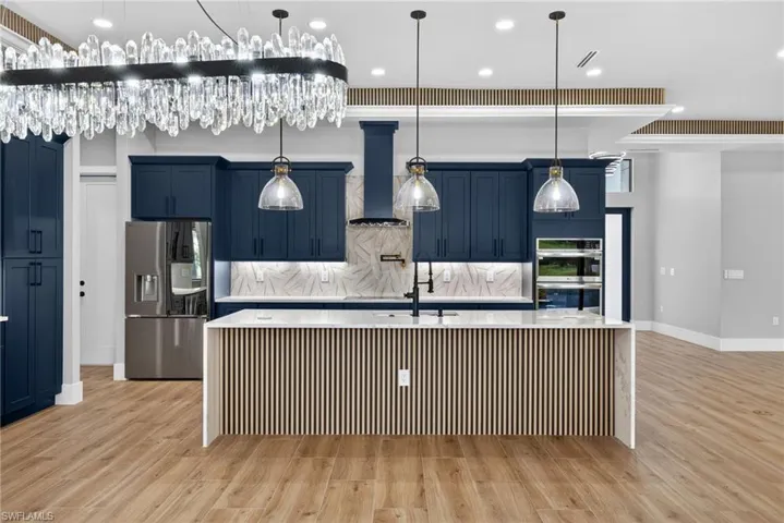 Kitchen with blue cabinetry, a spacious island, backsplash, appliances with stainless steel finishes, and light stone countertops