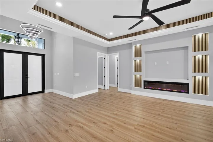 Unfurnished living room with light wood-style floors, french doors, a glass covered fireplace, a raised ceiling, and a ceiling fan
