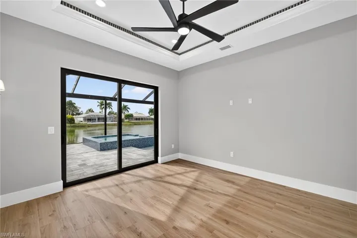 Primary bedroom with a sunroom, a water view, light wood finished floors, a raised ceiling, and a ceiling fan