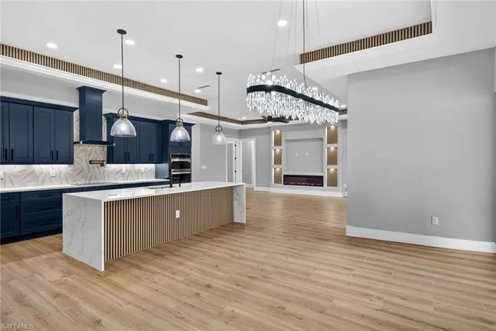 Kitchen with double oven, decorative light fixtures, backsplash, a center island with sink, and light wood-style flooring