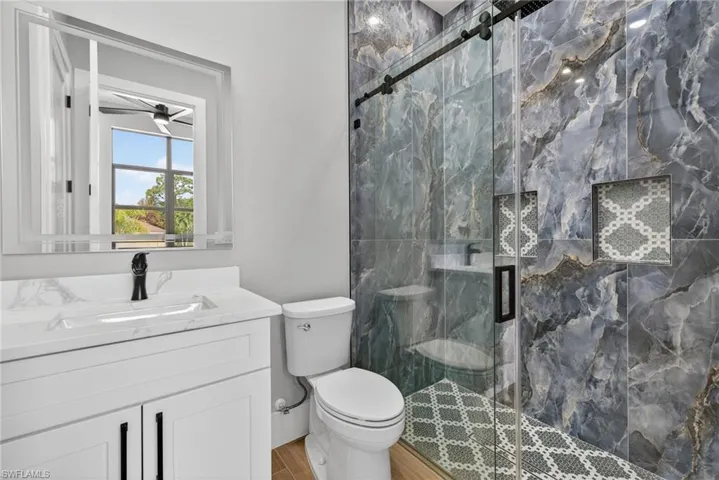 Full bath featuring a marble finish shower, vanity, and a ceiling fan