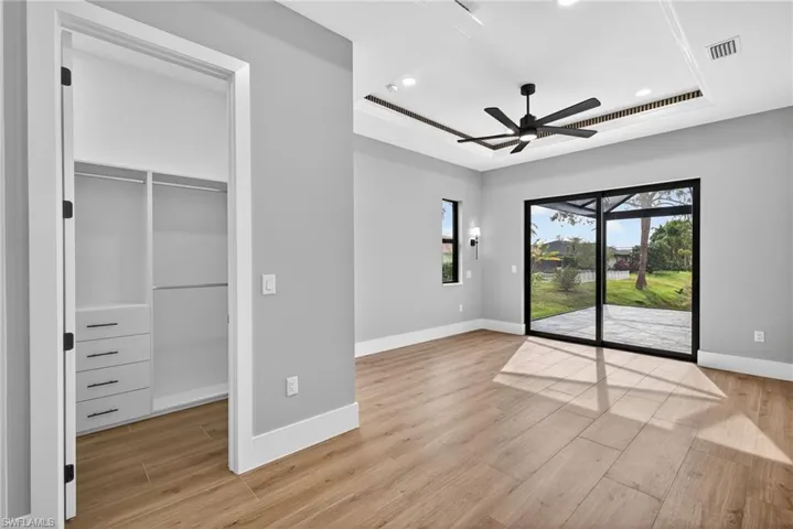 Primary bedroom featuring a raised ceiling, access to exterior, a walk in closet, light wood finished floors, and recessed lighting