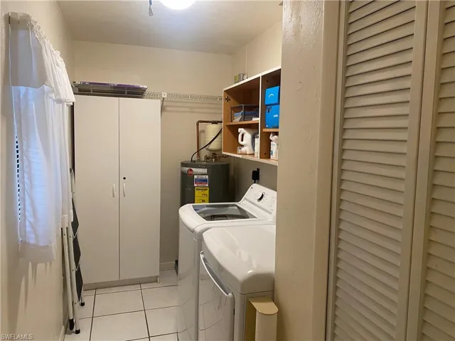 Clothes washing area with light tile patterned flooring, gas water heater, cabinets, and washing machine and clothes dryer