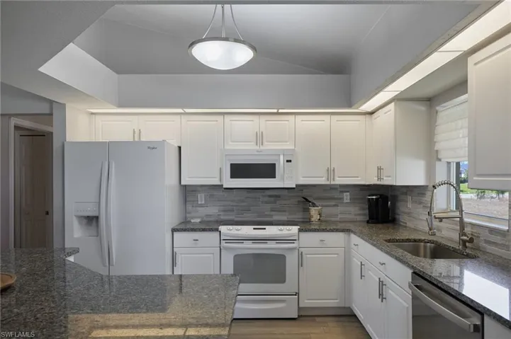 Kitchen with white appliances, dark stone counters, white cabinetry, decorative backsplash, and vaulted ceiling