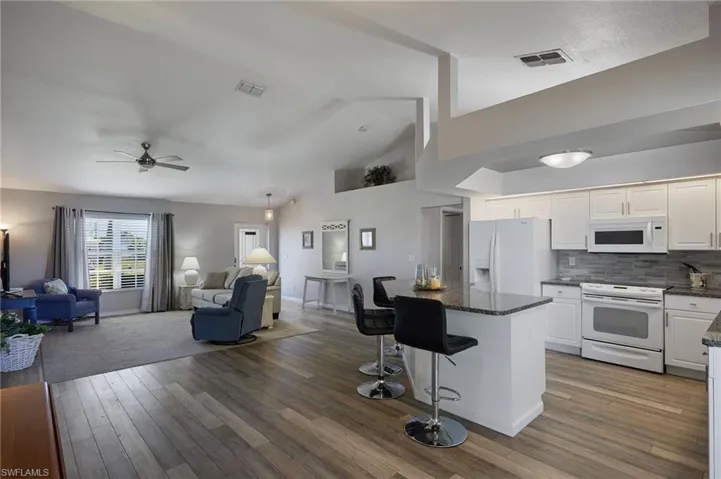 Kitchen featuring white appliances, open floor plan, a kitchen bar, a kitchen island, and high vaulted ceiling