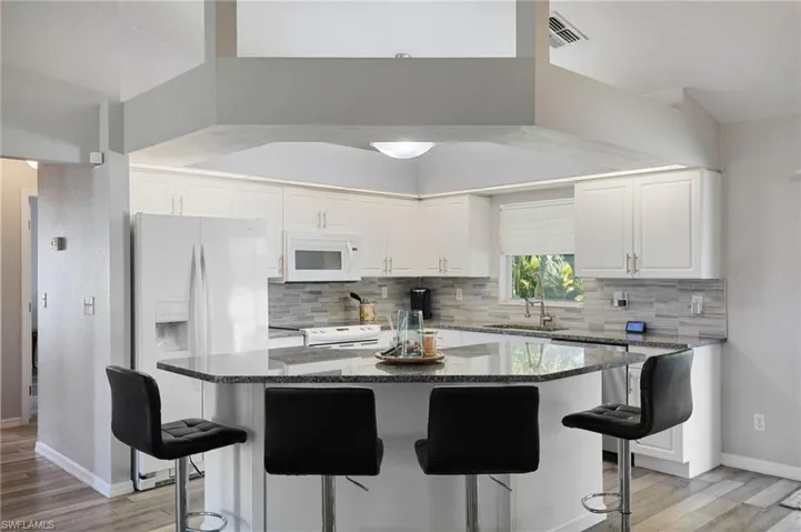 Kitchen featuring a kitchen breakfast bar, a kitchen island, dark stone countertops, white appliances, and vaulted ceiling