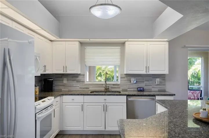 Kitchen with white appliances, dark stone countertops, and white cabinets