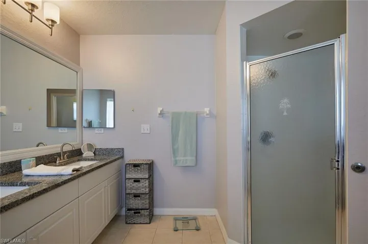 Full bath with double vanity, a shower stall, light tile patterned flooring, and a textured ceiling