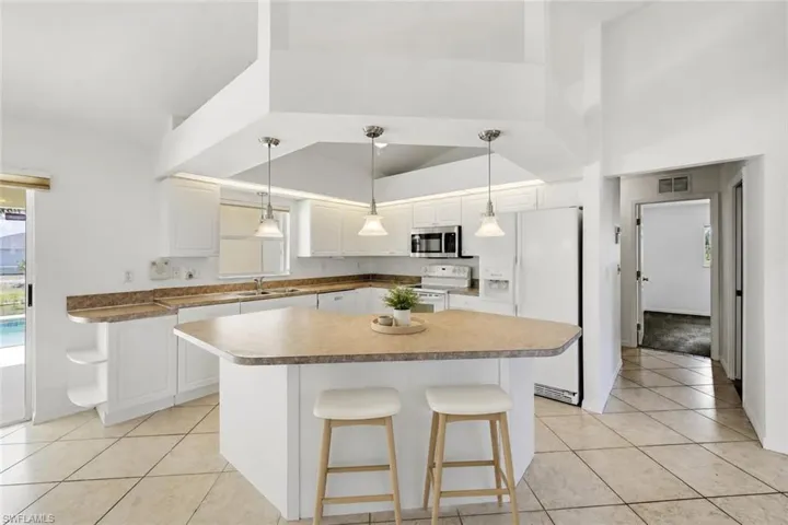 Spacious kitchen featuring an angular island, white cabinetry, integrated appliances, and pendant lighting