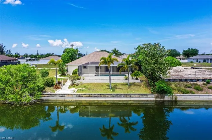 Waterfront property featuring a screened-in pool area, mature palm trees, a concrete seawall, and a private dock