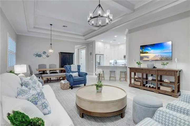 Living room featuring light hardwood / wood-style floors, crown molding, a notable chandelier, a raised ceiling, and sink