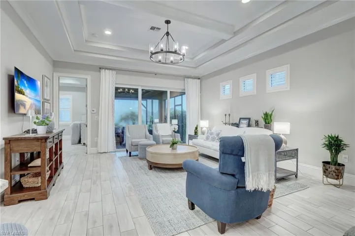 Living room with a healthy amount of sunlight, a chandelier, beam ceiling, and a raised ceiling