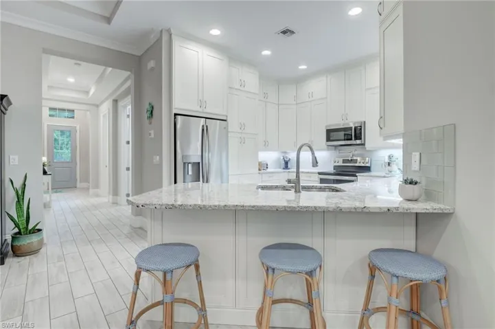 Kitchen with backsplash, a raised ceiling, light stone countertops, white cabinets, and appliances with stainless steel finishes