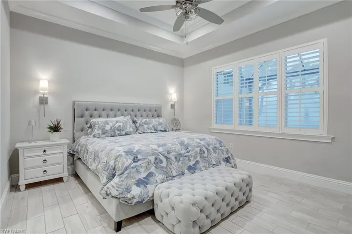 Bedroom with light hardwood / wood-style floors, ceiling fan, and a tray ceiling