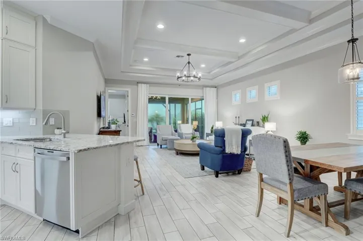 Kitchen with stainless steel dishwasher, white cabinets, light stone counters, backsplash, and sink