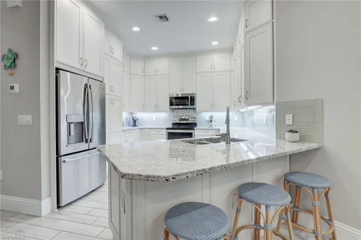 Kitchen featuring backsplash, appliances with stainless steel finishes, white cabinetry, and kitchen peninsula