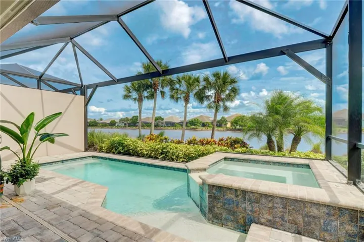 View of pool with screened enclosure, an in ground hot tub, and a water view