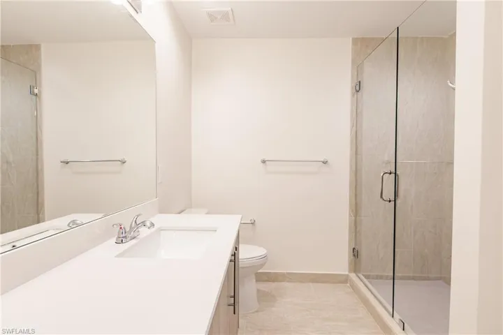 Primary bathroom featuring a shower with door, tile flooring, toilet, and oversized vanity