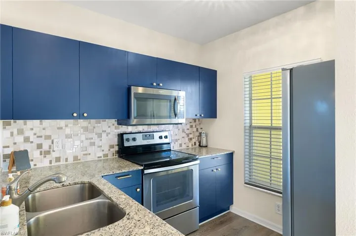 Kitchen with appliances with stainless steel finishes, light stone counters, dark wood-type flooring, sink, and blue cabinetry
